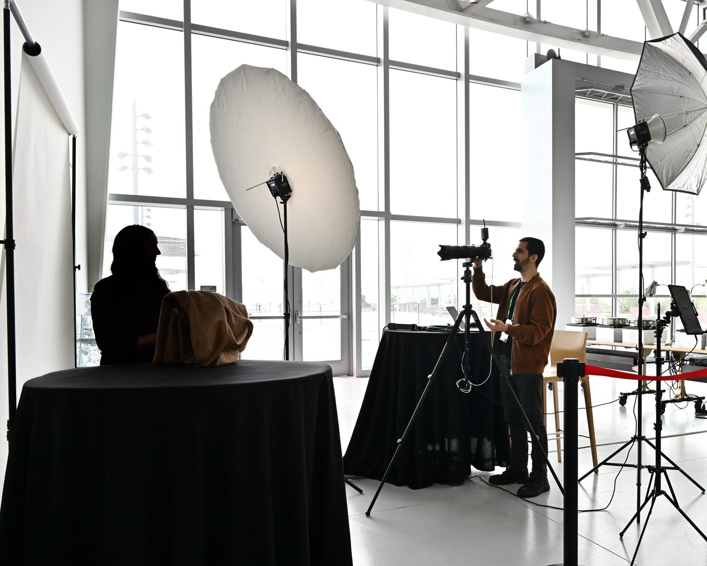 Nir directing a guest at the booth, with a large umbrella light and a white seamless backdrop.